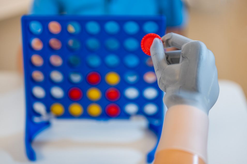 Training des Feingefühls mit einer Handprothese. Ein Mann hält einen roten Spielstein mit seiner Handprothese beim Spiel «Vier gewinnt».