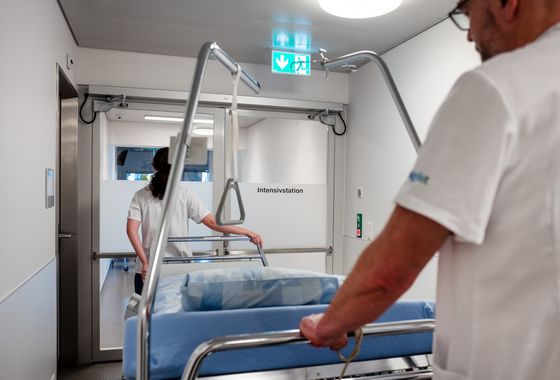 Zwei Mitarbeitende transportieren ein Patientenbett auf die Intensivstation. Zwei Mitarbeitende transportieren ein Patientenbett auf die Intensivstation.